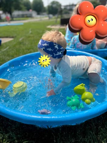 Reviewer's toddler wearing swimming headband with shark design and playing in pool