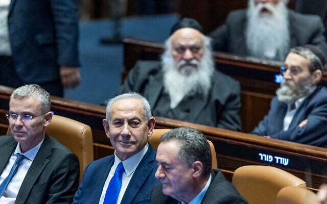 Prime Minister Benjamin Netanyahu (center), Justice Minister Yariv Levin (left), and Defense Minister Israel Katz (right), with ultra-Orthodox MKs Yitzchak Goldknopf, Moshe Gafni and Meir Porush behind them, seen in the Knesset shortly before the vote on a law banning arrests of ultra-Orthodox draft dodgers and legitimizing ongoing mass ultra-Orthodox non-enlistment, July 14, 2026. (Chaim Goldberg/Flash90)