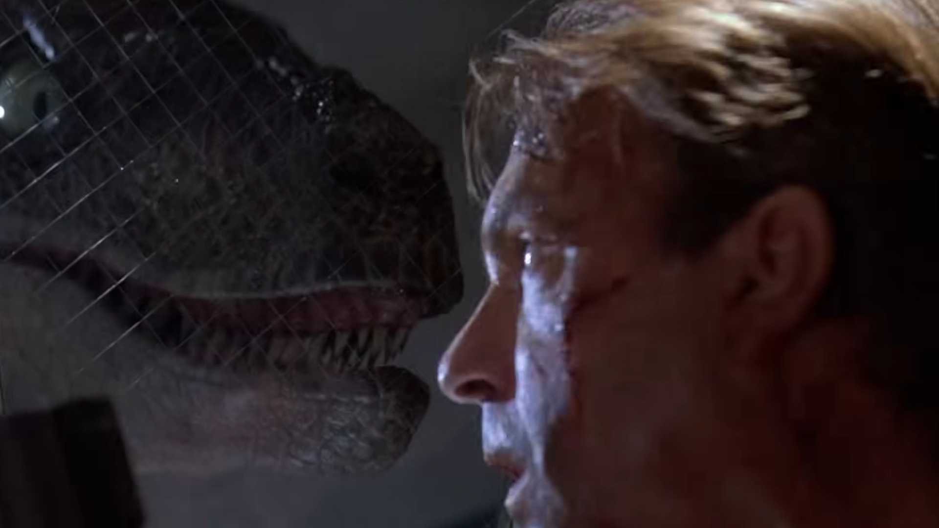 Dr Grant and a raptor lock eyes through the glass in Jurassic Park