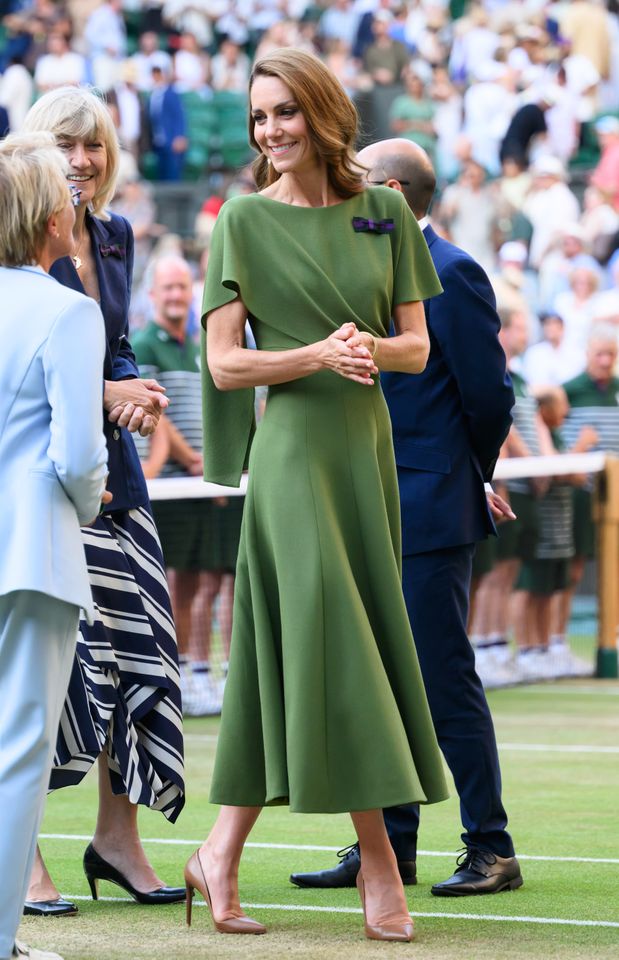 A woman stands on a tennis court wearing a formal green dress in conversation with others