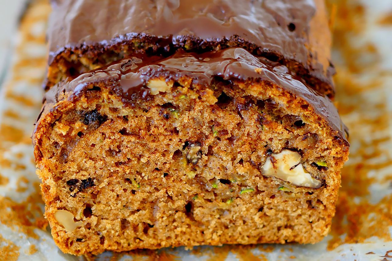 looking into a perfect slice of zucchini bread with the rest of the loaf directly behind and both are topped with chocolate.
