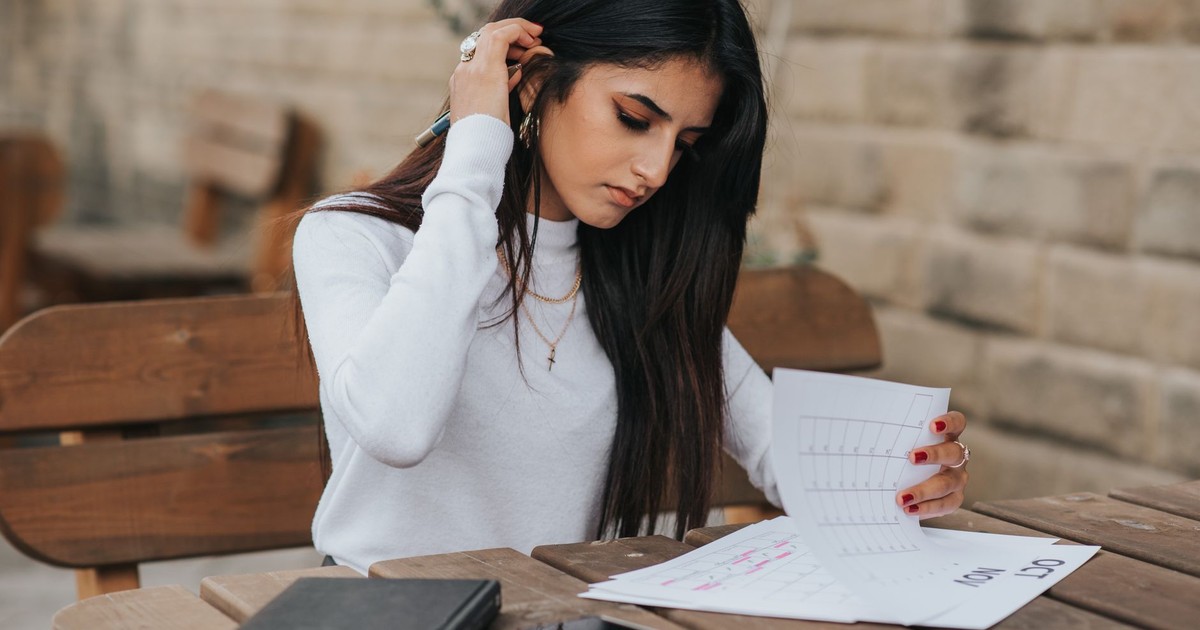 Young ethnic female student in casual outfit with dark hair at wooden table looking through plans in calendar