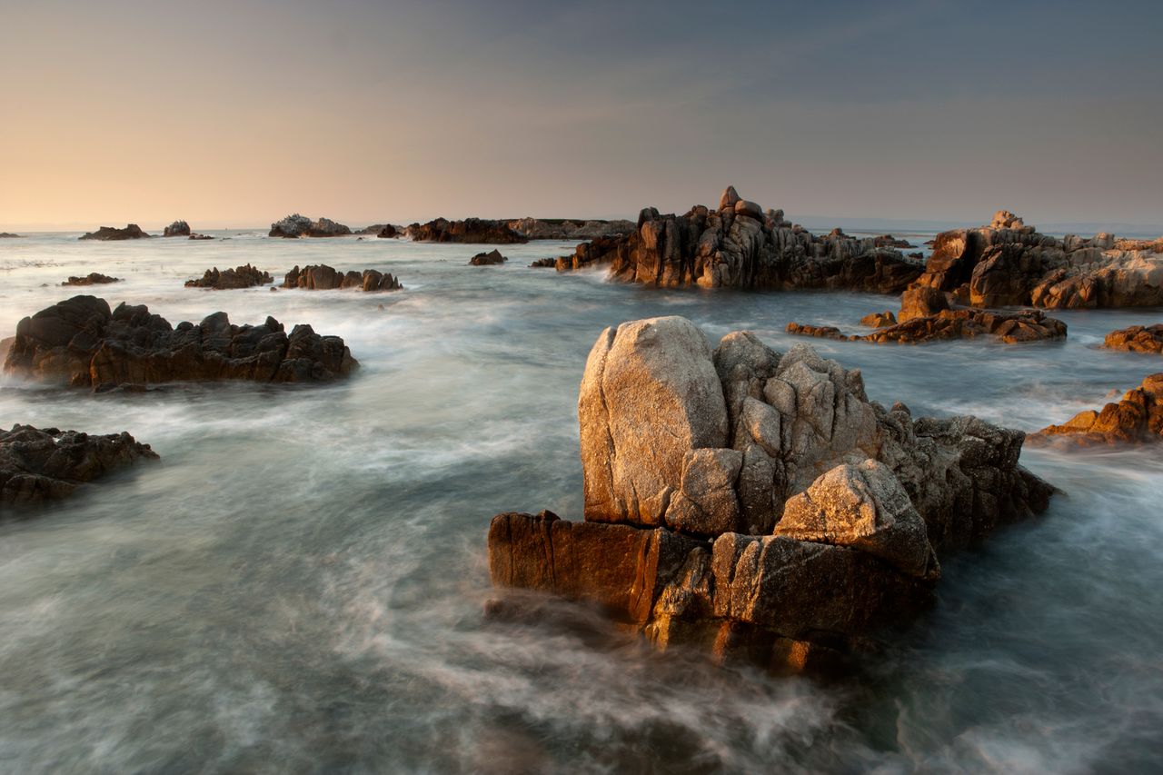 Rocky shoreline with waves at Asilomar State Beach during sunset