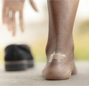Close-up of a foot with a blister bandage on the heel, shoe in the background, illustrating a product for foot protection