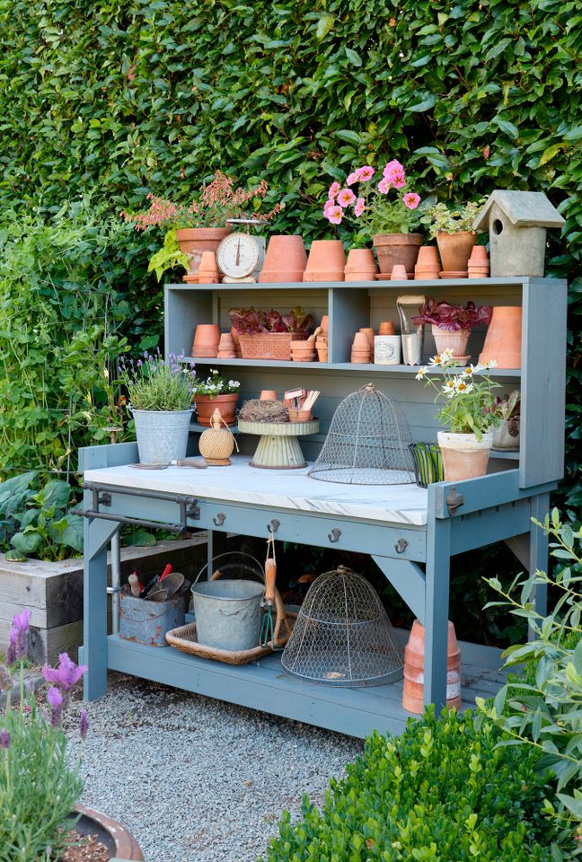 A garden potting bench with gardening tools pots and plants arranged neatly in a garden setting