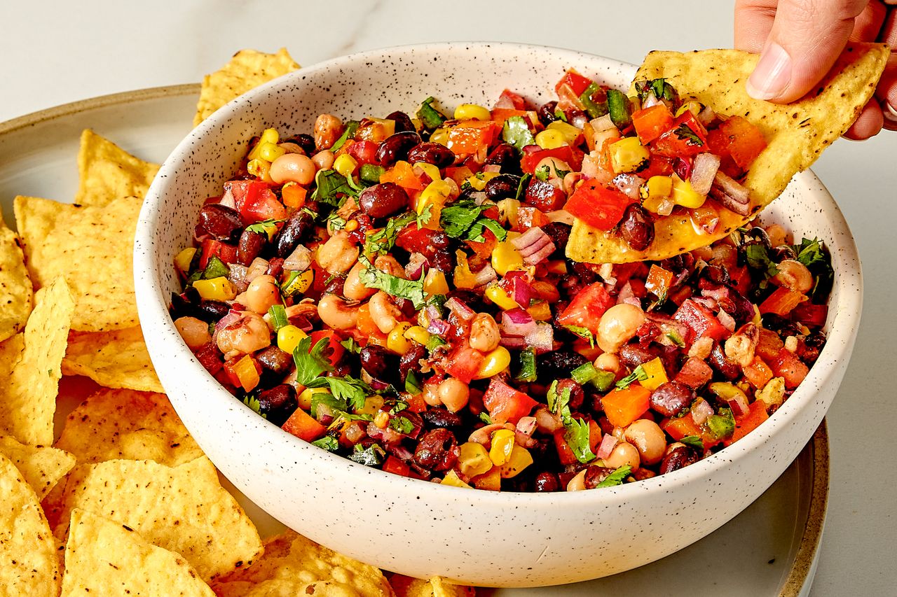 A bowl of cowboy caviar with a tortilla chip being dipped in
