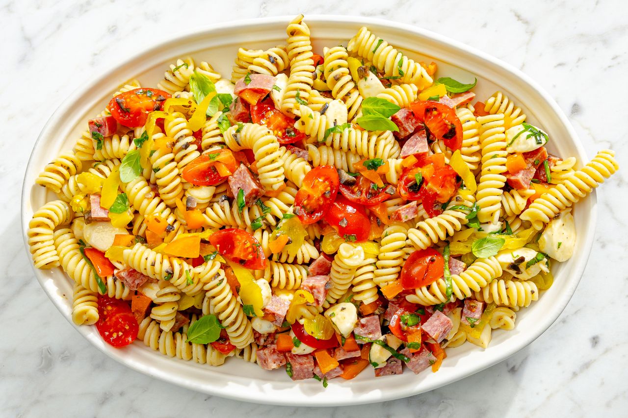 A plate of pasta salad with fusilli vegetables and small cuts of cured meats garnished with herbs