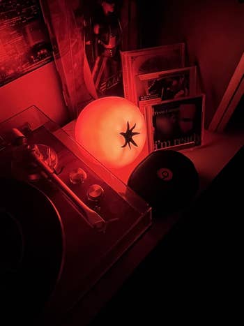 Glowing tomato-shaped lamp on a shelf with vinyl records and a turntable, creating a cozy atmosphere