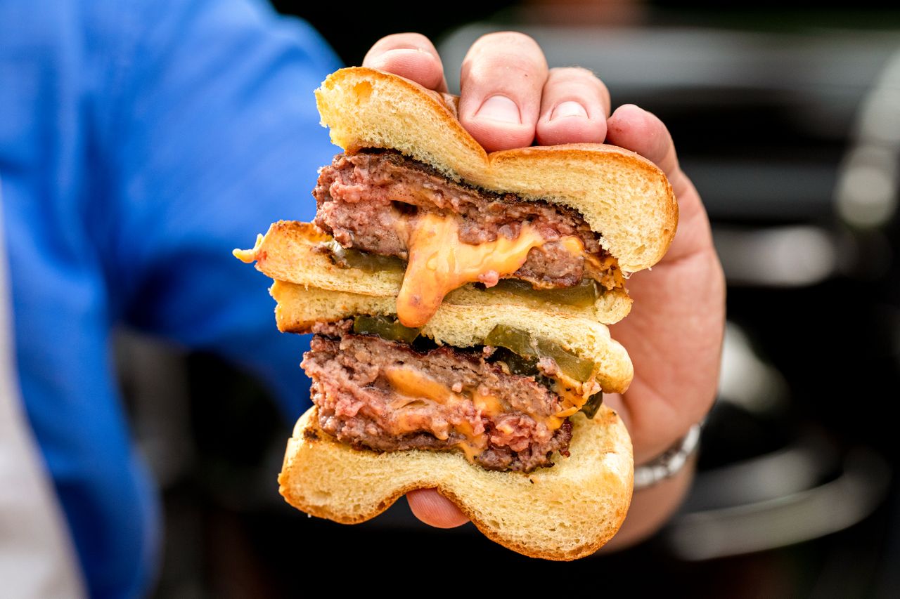 A hand holding a halved cheeseburger with melted cheese inside