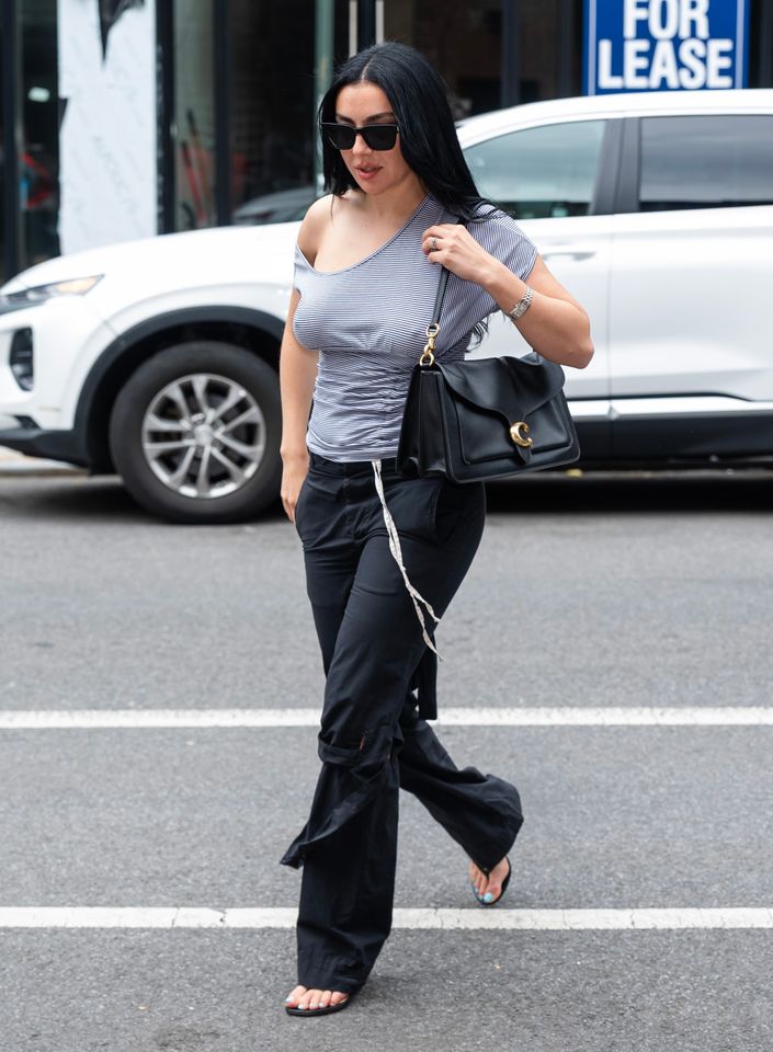 Charli xcx walking on a street carrying a black handbag and wearing casual attire