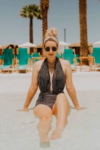 Reviewer wearing low fitted bathing suit sitting in shallow water at beach