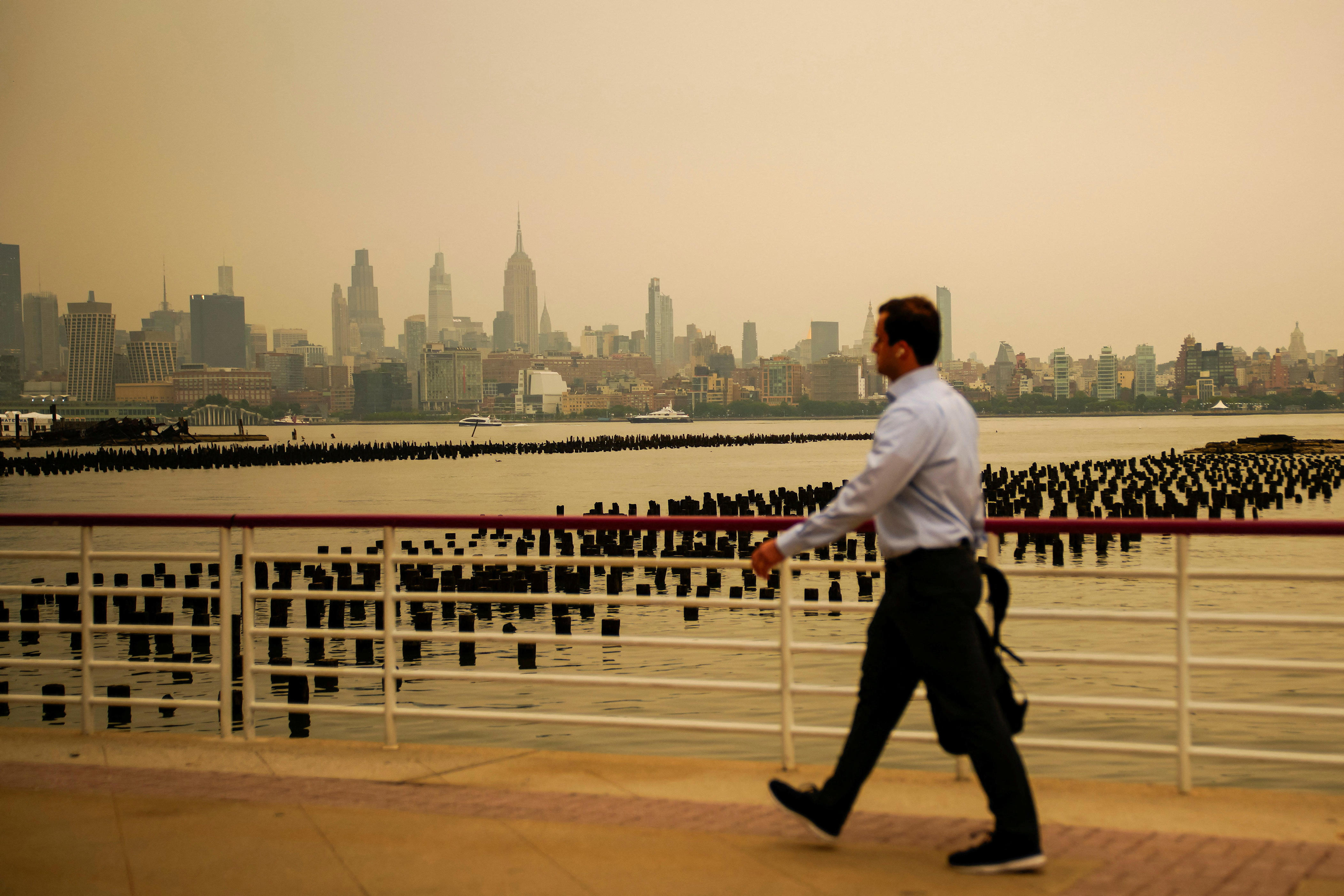 A man walks while the New York City skyline and the Empire State Building are seen through a cover of wildfire smoke, as pictured from Newport, New Jersey, on July 16, 2026.