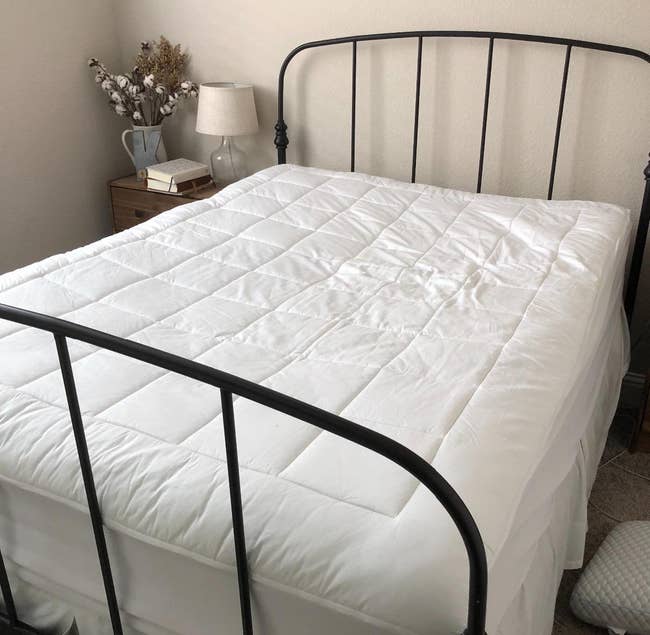 room with a bed with a mattress topper, minimal decor, and a bedside lamp