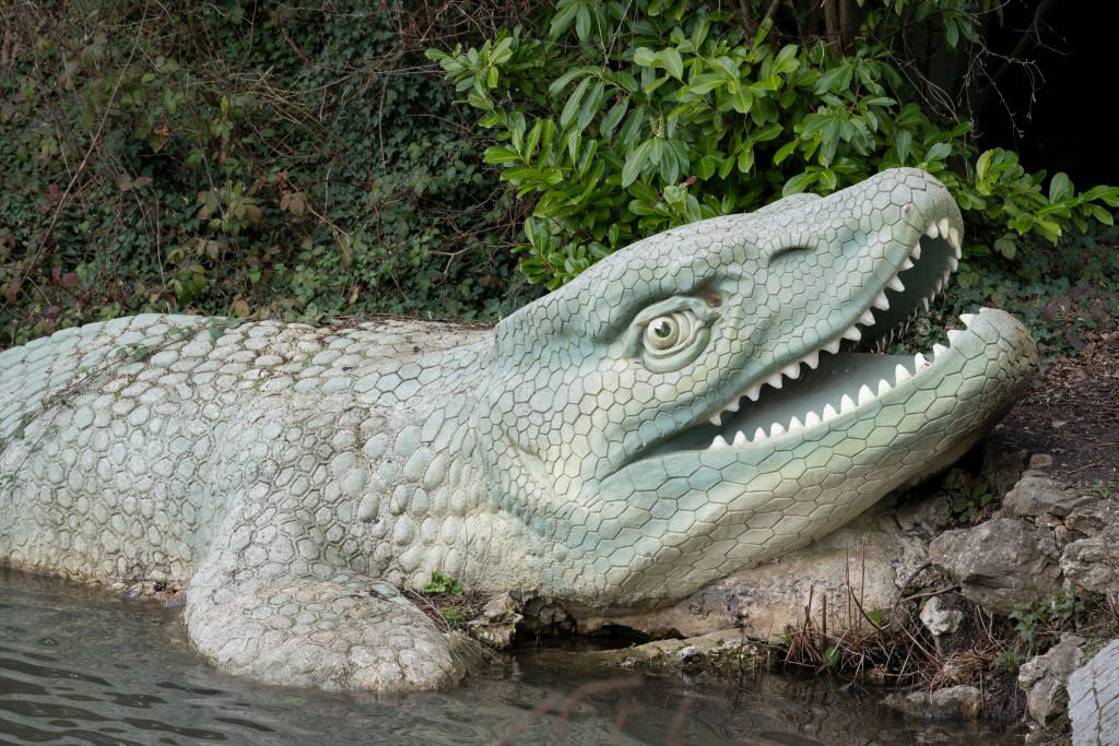 A park landscape of Victorian-era Grade I-listed dinosaur sculptures in Crystal Palace Park.