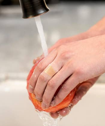 Hands washing an apple under running water with a bandage on one finger