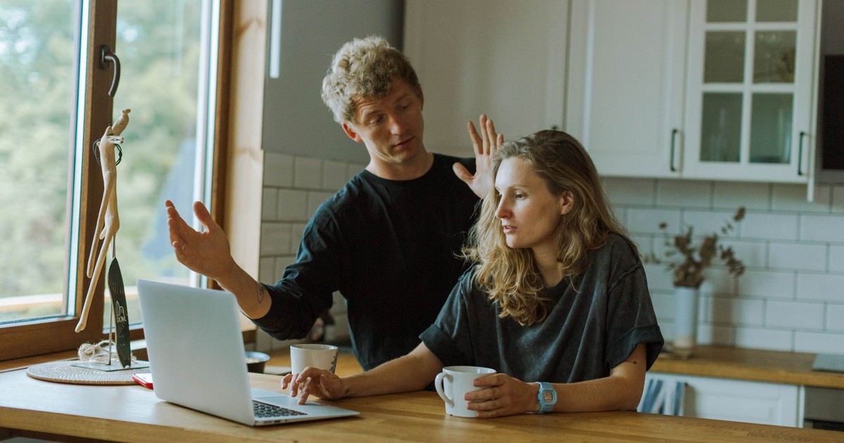 A couple interacting in a bright kitchen using a laptop at a wooden counter.