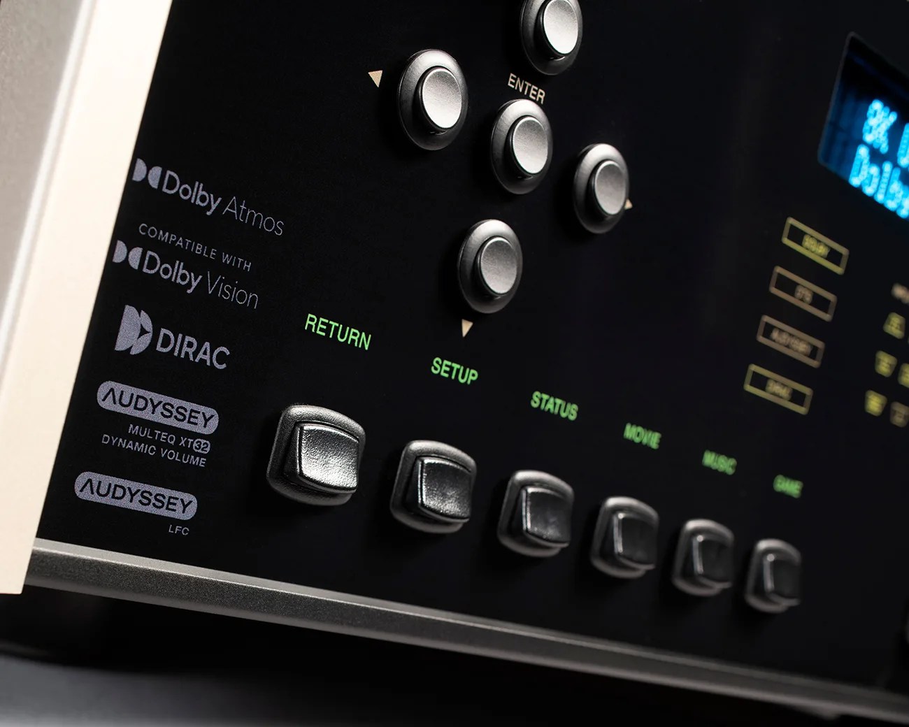 Close-up of a black audio receiver panel with silver buttons and logos for Dolby Atmos, Dolby Vision, DIRAC, and Audyssey.