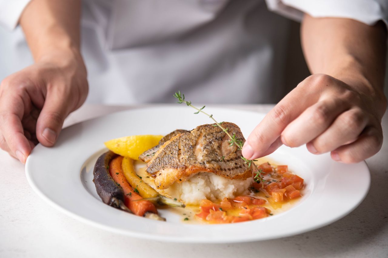 Chef garnishing a plated fish dish with vegetables
