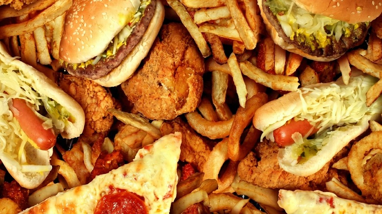 A jumble of fast food items including hamburgers, french fries, fried chicken, pizza, and hot dogs