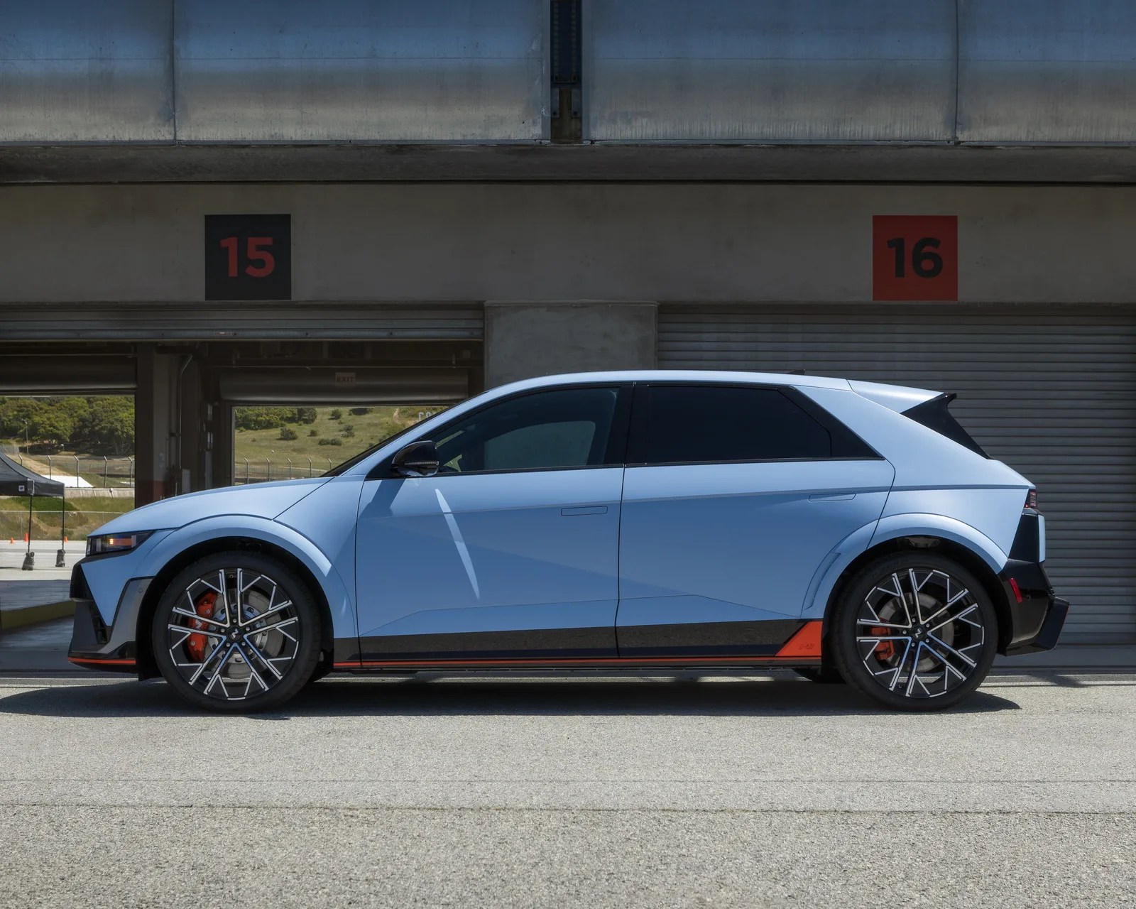 Light blue compact electric hatchback car with black and orange accents parked in front of numbered garage doors.