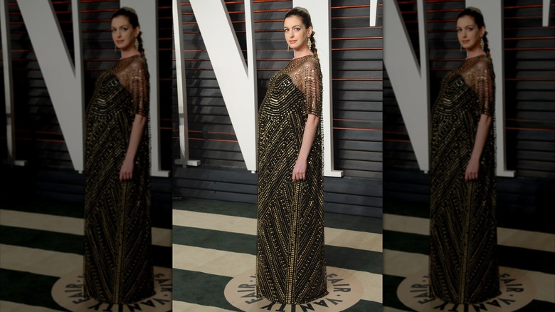 Anne Hathaway poses in a black-and-gold dress that shows off her baby bump