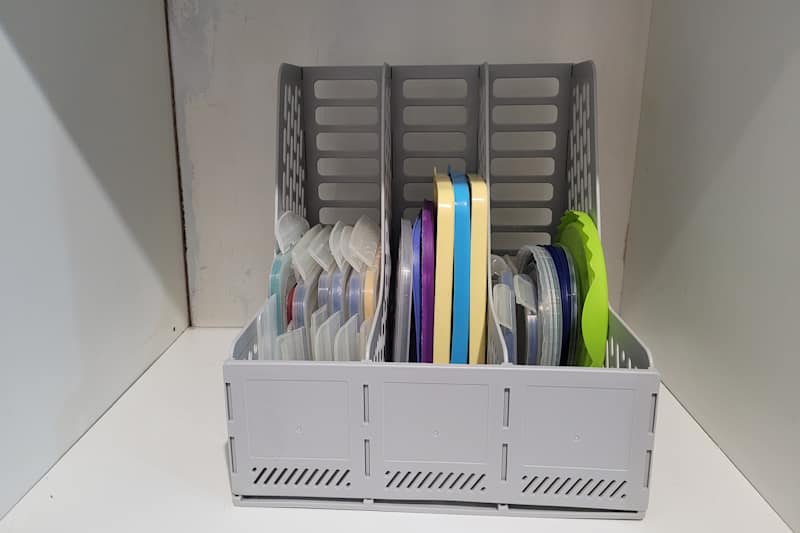 Container holding various colored lids organized in a gray basket with dividers, placed on a white surface.
