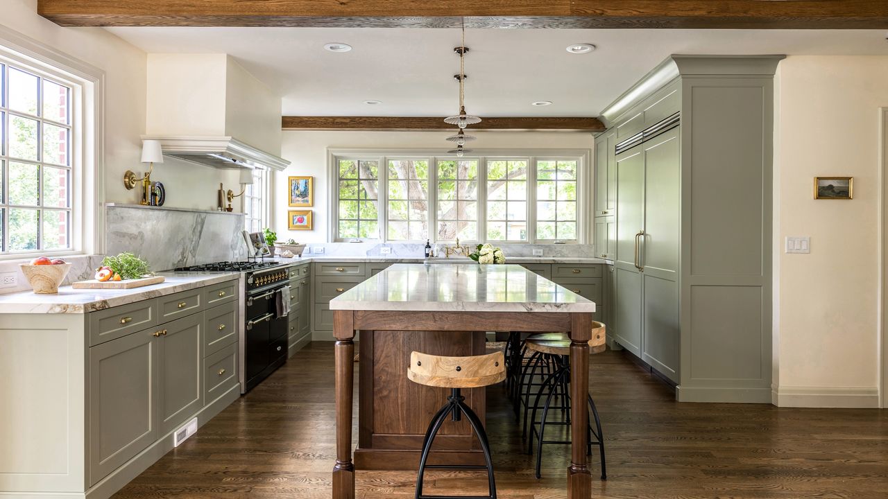 A U-shaped kitchen with cabinets painted in French Gray by Farrow and Ball, marble countertops, brass hardware, and a wooden island