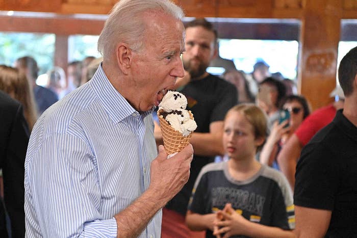 A person enjoying an ice cream cone in a crowded setting, wearing a collared shirt, with people and activity in the background