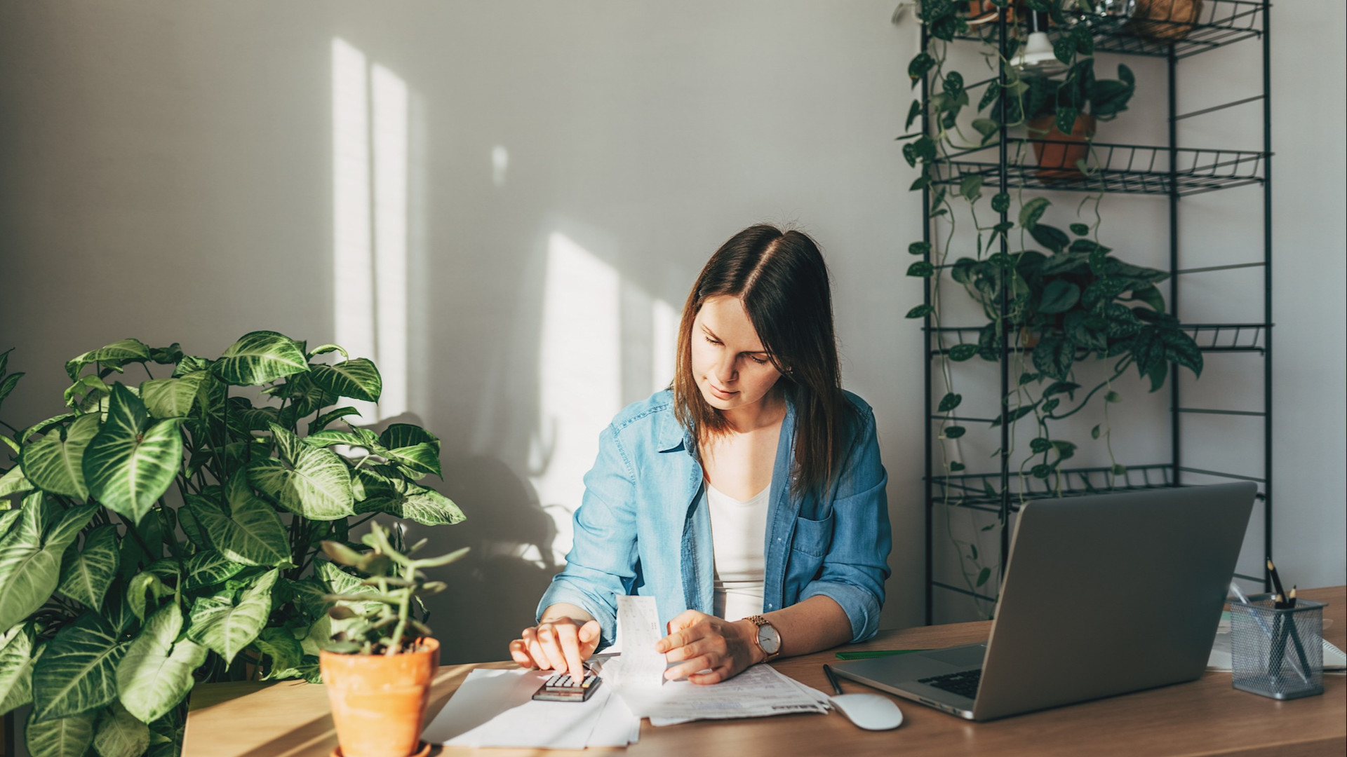 Discover a woman doing her taxes at home, surrounded by plants as she reviews documents and focuses on organizing