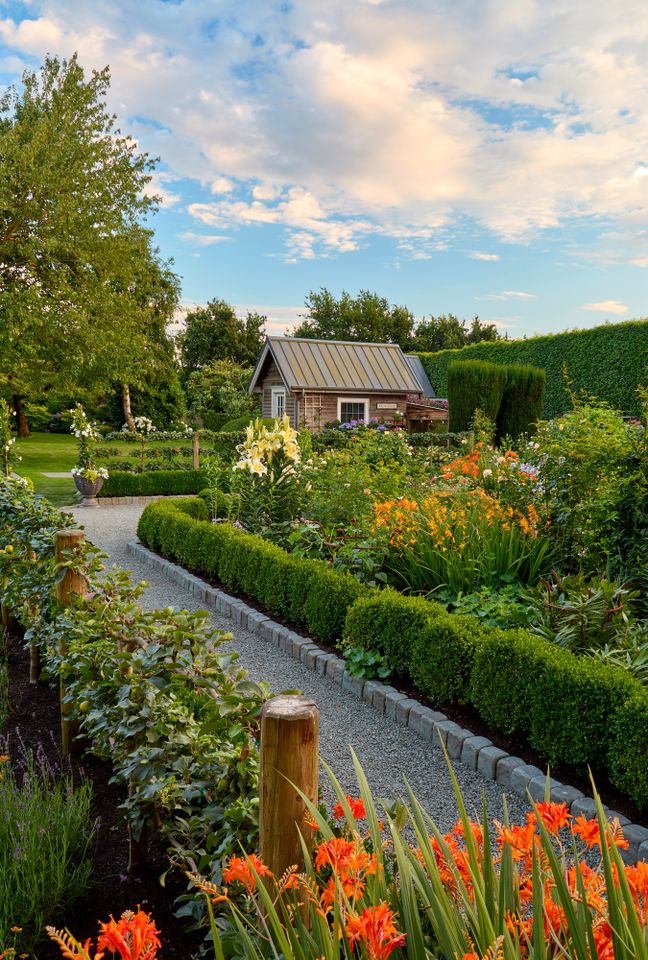 A landscaped garden with a pathway flowerbeds and a cottage in the background
