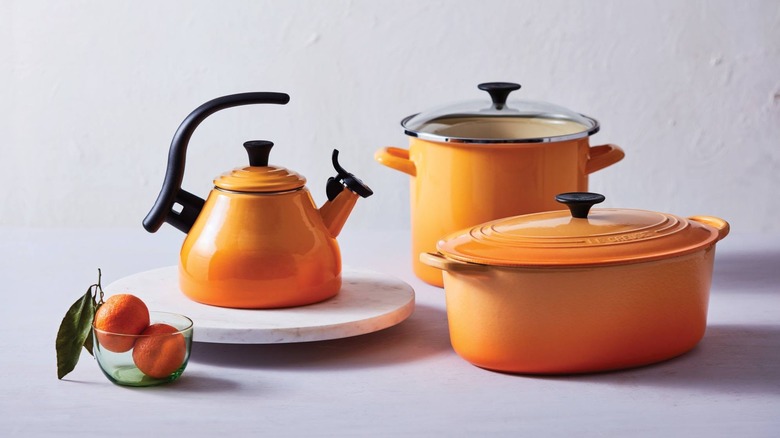 A Le Creuset teapot, oval Dutch oven, and stockpot all in Orange Blossom