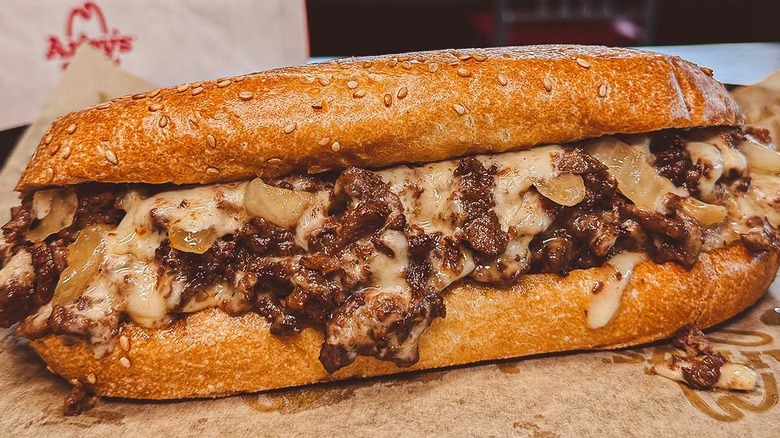 An Arby's Angus Cheesesteak loaded with steak, cheese, and onion on a sesame seed bun