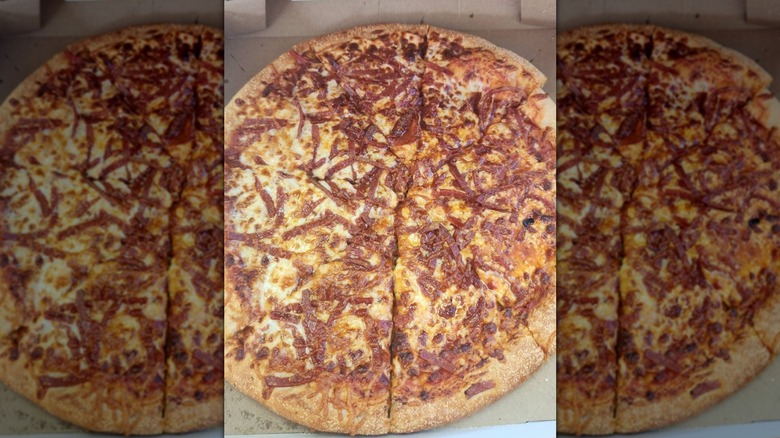 A pizza in a box featuring golden cheese and a tangle of shredded pepperoni covering it