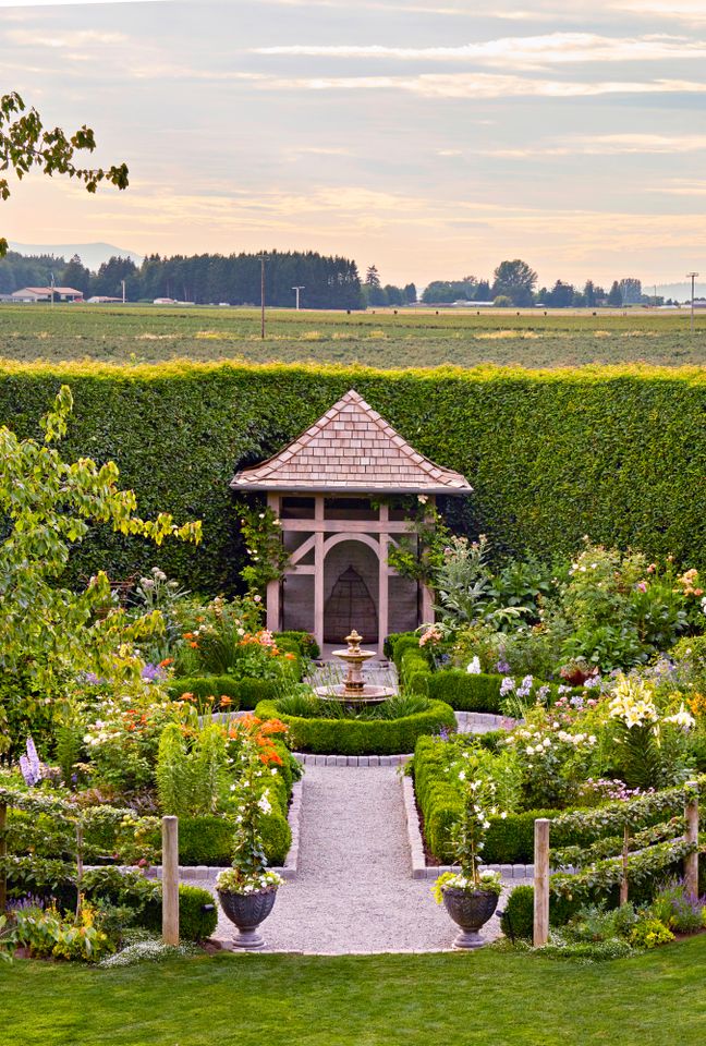 A neatly designed garden with a central path symmetrical flower arrangements and a gazebo at the end