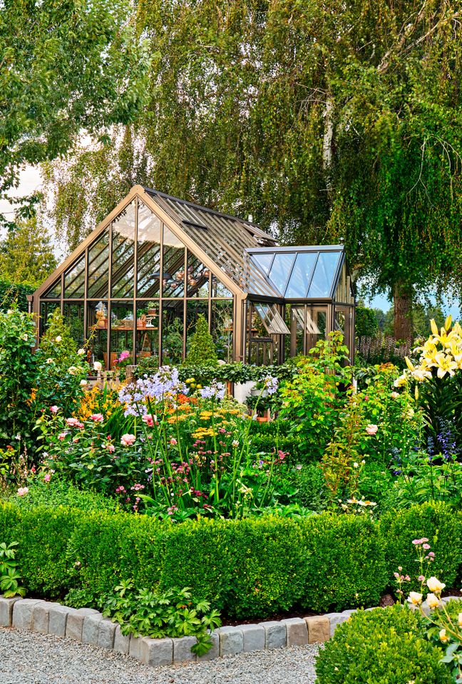 A wooden greenhouse surrounded by a wellmaintained garden with various plants and flowers