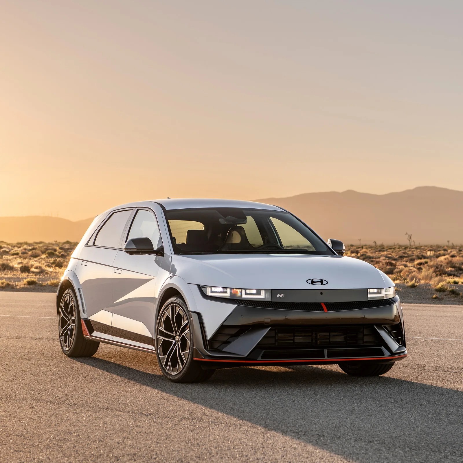 White Hyundai Ioniq 5 electric car with black and red accents parked on a desert road at sunset.