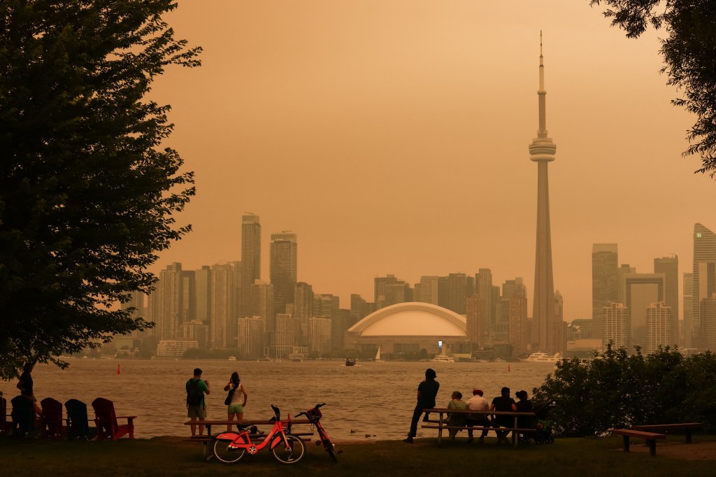 People look toward the downtown skyline from the Toronto Islands as forest fires in Northern Ontario cause poor air quality over the city, in Toronto, Ontario, Canada, July 15, 2026. Toronto had the worst air quality of any major city in the world on Wednesday, the Swiss firm IQAir said, as Canadian authorities urged people to stay indoors. Toronto edged out New Delhi and the Democratic Republic of Congo's capital Kinshasa as wildfire smoke turned the skies a hazy yellowish-grey in Canada's largest city. (Photo by Cole BURSTON / AFP via Getty Images)