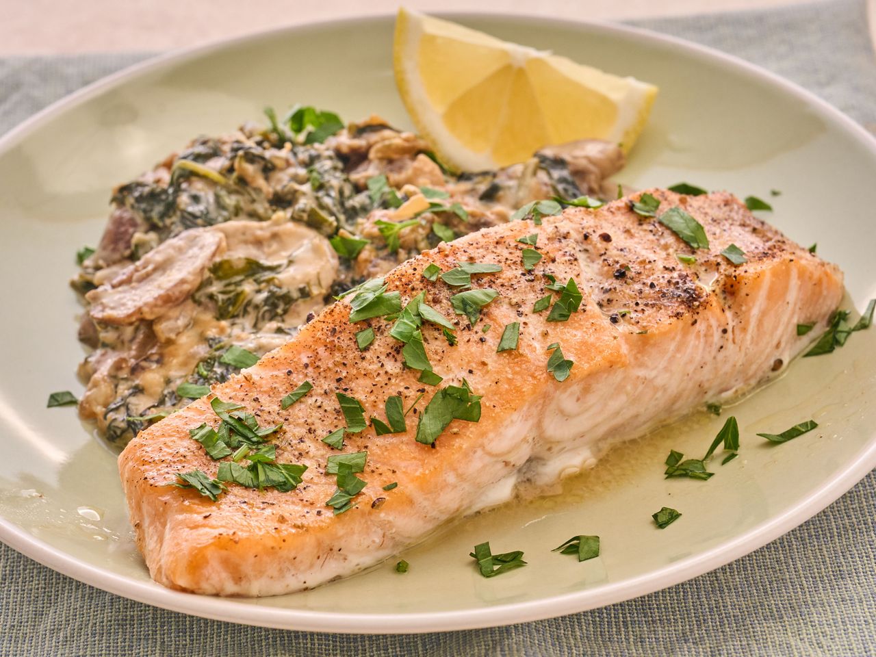 Salmon fillet with sides on a plate garnished with herbs and served with a lemon wedge and spinach mixture