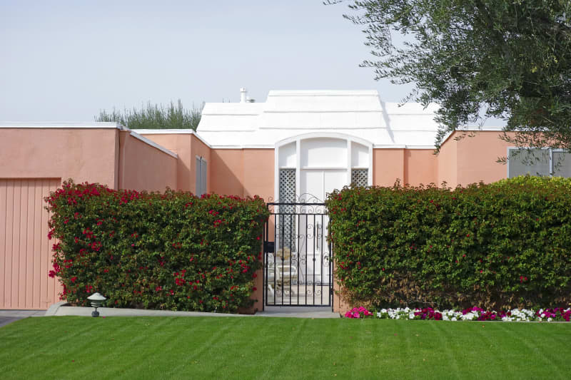 Pink and white gated and walled Mid Century Style townhouse. Garden of Petunias and Bougainvillea with lawn.