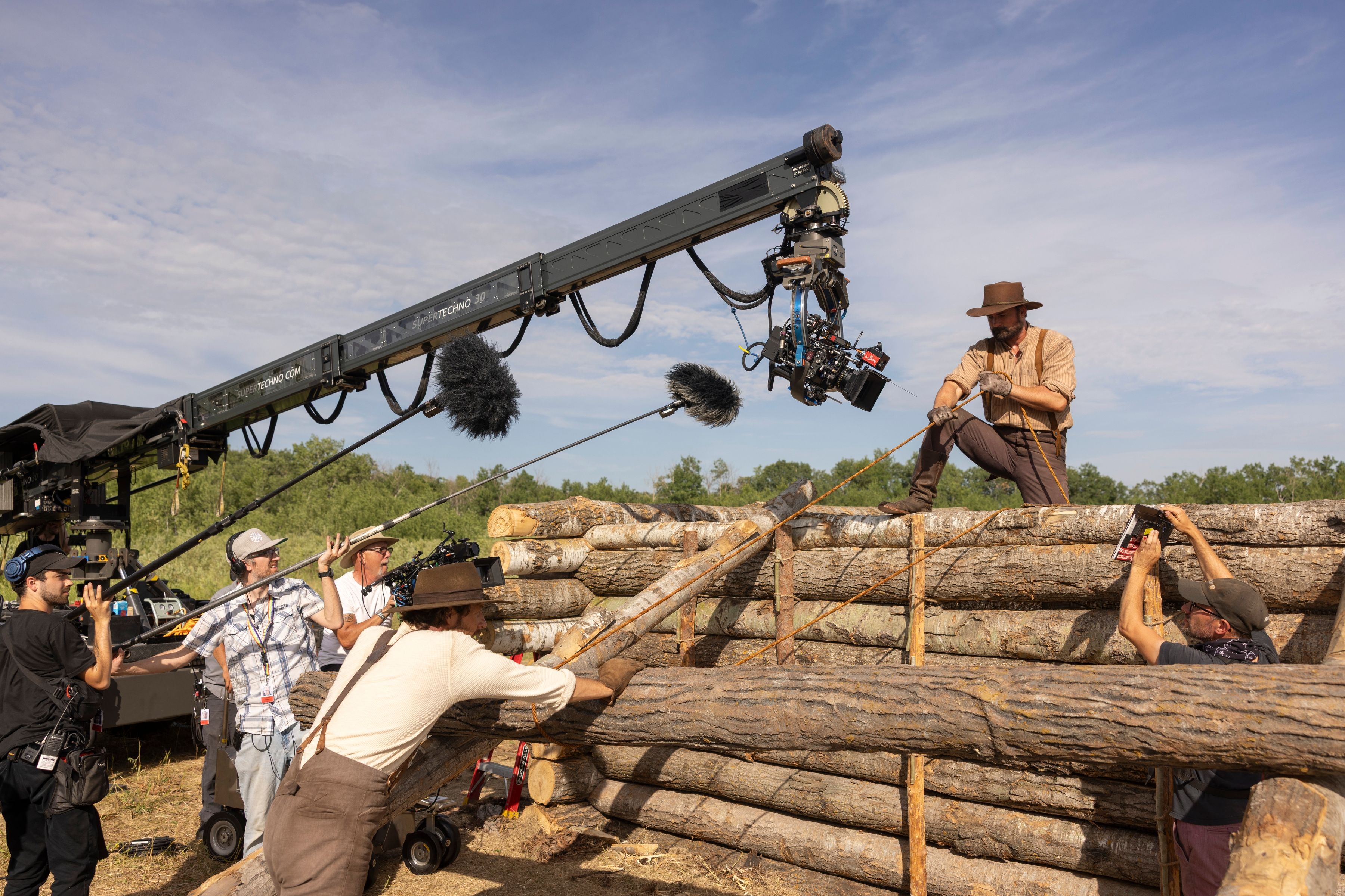 Luke Bracey as Charles Ingalls and Warren Christie as John Edwards are shown here pulling a log cabin together on set. The crew used wooden pegs instead of nails to construct the Ingalls family’s log cabins in order to stay authentic to the Little House time period.