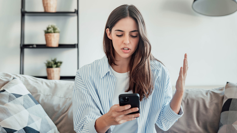 Woman looking at phone and making frustrated gesture