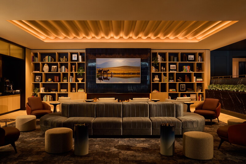 A living room–like area in the Chase Sapphire Lounge at DFW airport with a large bookshelf, a hanging frame depicting horses, and an oval couch and seats all around
