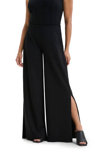 Person wearing a sleeveless black jumpsuit with wide-leg pants and side slits, paired with open-toed sandals