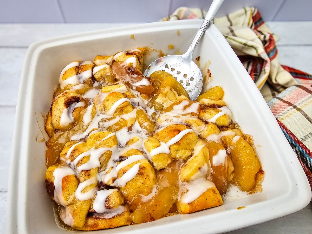 Baked apple pie cinnamon rolls in a white square dish with icing drizzle