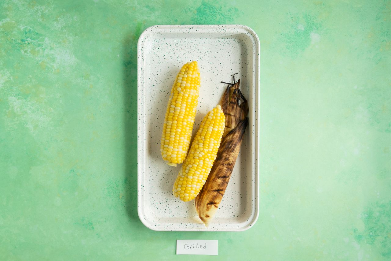 Three pieces of grilled corn on the cob on a rectangular tray with a green background