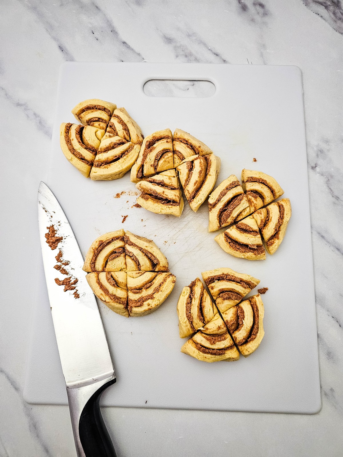 Canned cinnamon rolls cut into quarters on a white cutting board
