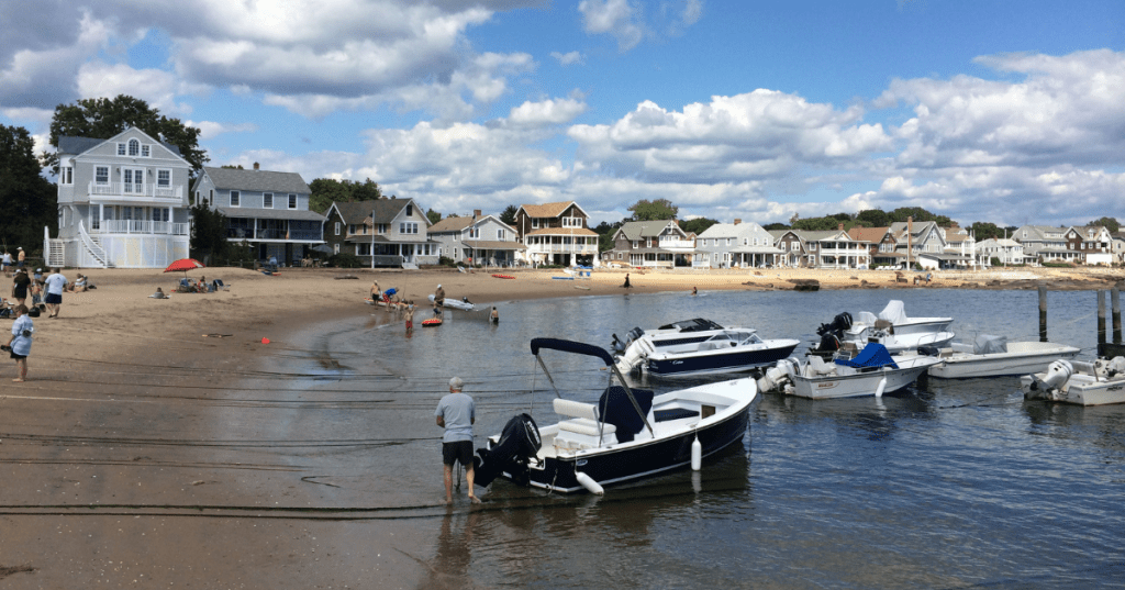 people on the sand and boats moored in the water at a beach in madison connecticut