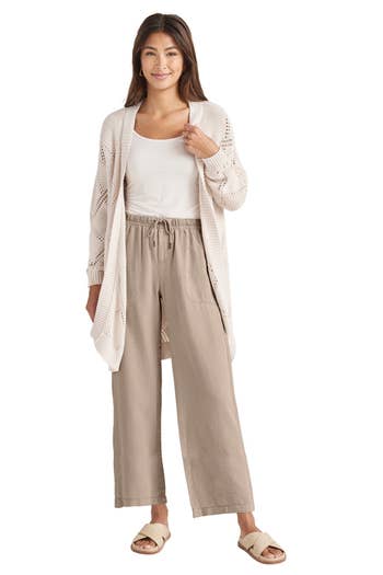 Woman wearing a light cardigan, white top, and loose pants, modeling casual wear suitable for shopping
