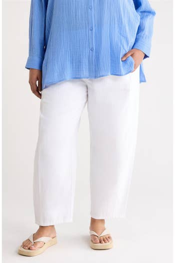 Person wearing a loose-fit, striped blouse, white pants, and sandals