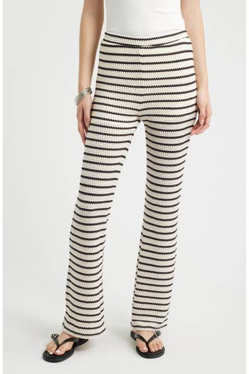 Woman modeling knit striped pants with flared legs, wearing black sandals and a bracelet, against a plain backdrop
